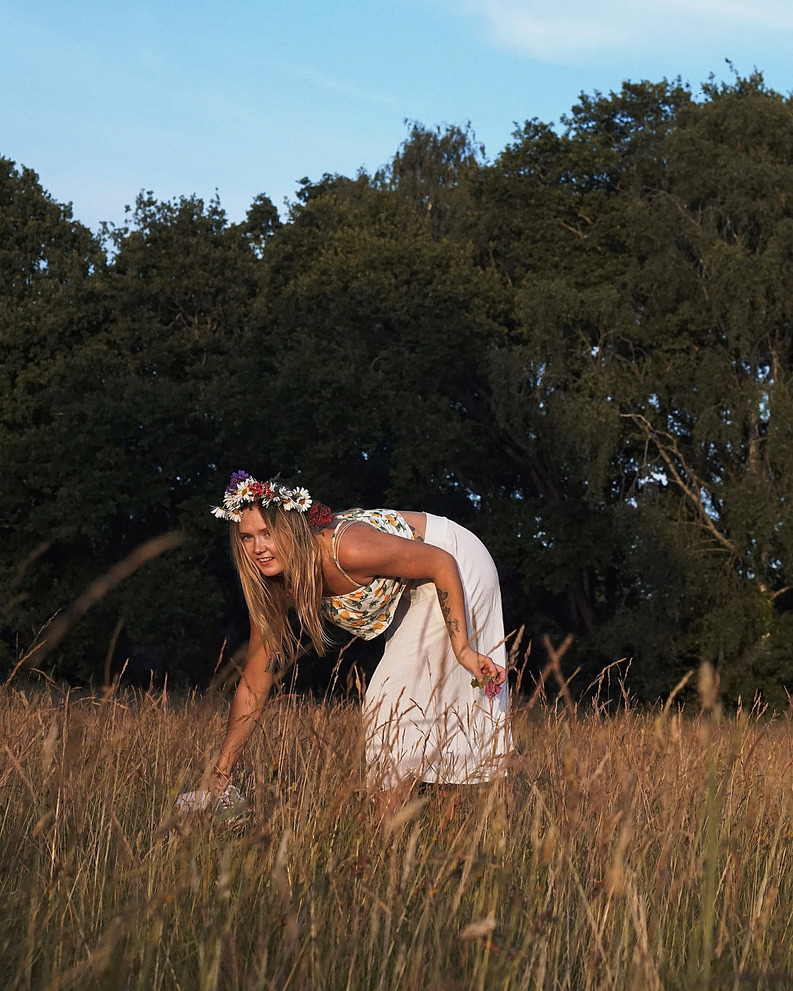 Woman in a meadow picking wildflowers at sunset, symbolising belonging and self-discovery.